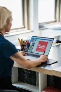 Blonde woman designing on laptop at modern desk in office setting.